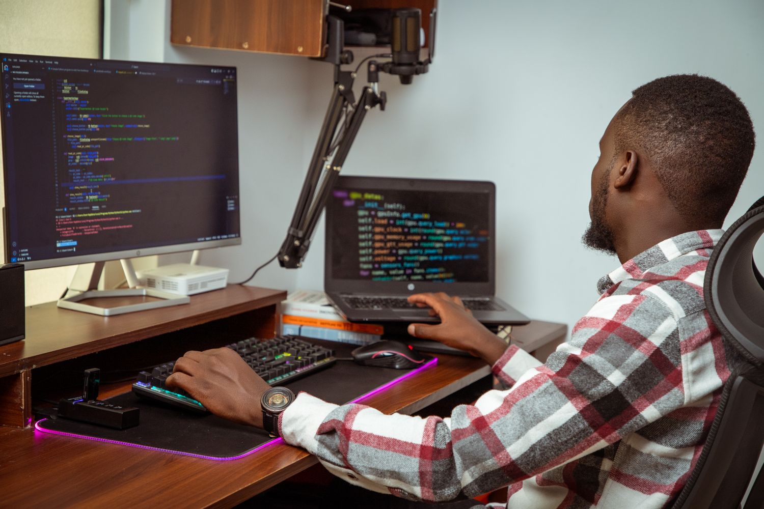 A developer writing code at a desk with a monitor and laptop